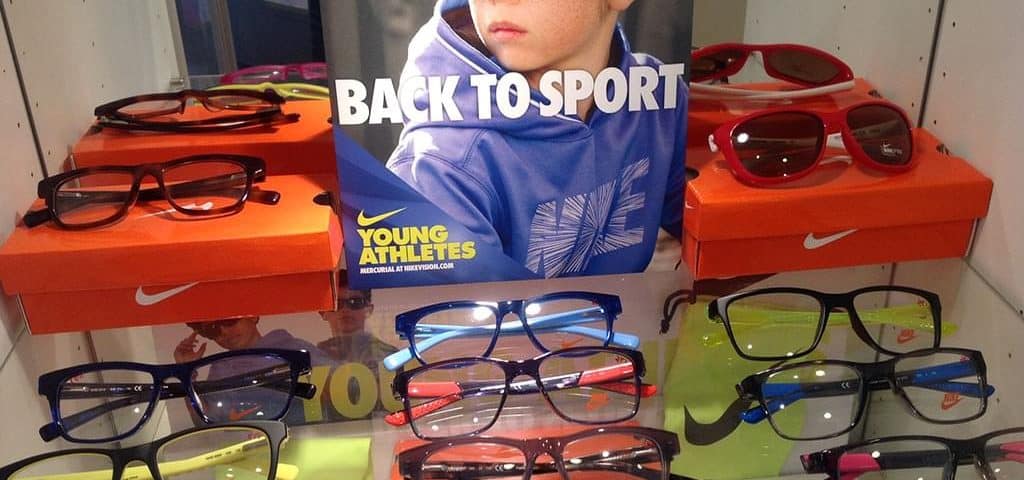 Child wearing sporty sunglasses for kids, surrounded by colorful frames and sports-themed display.