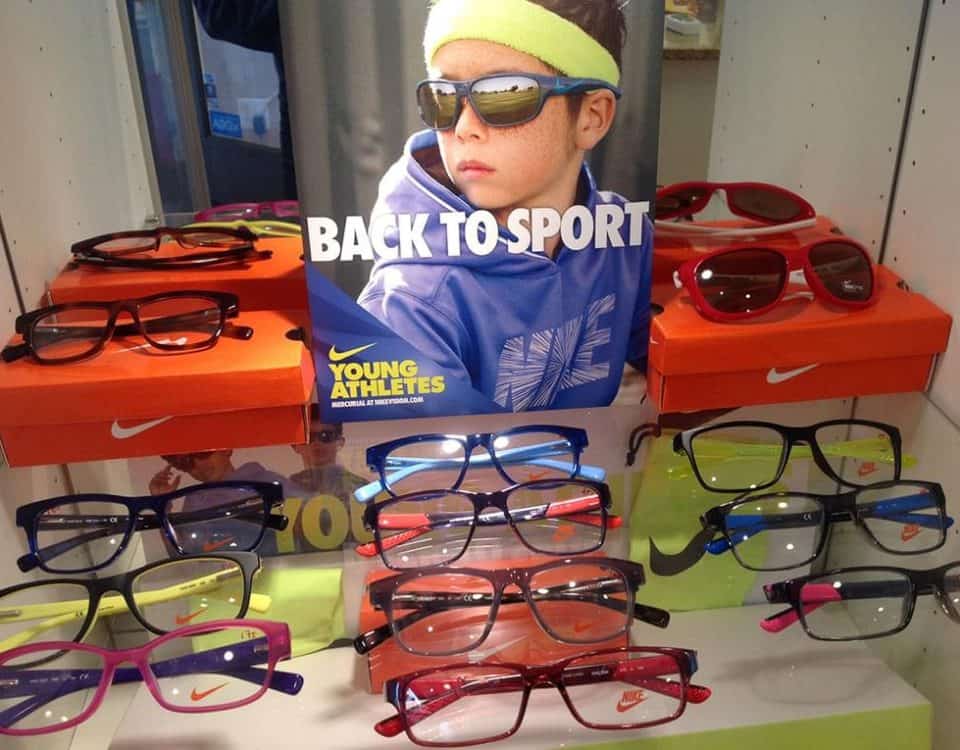 Child wearing sporty sunglasses for kids, surrounded by colorful frames and sports-themed display.
