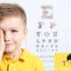 kid holding eye with hand with a blurred out eye exam behind him.